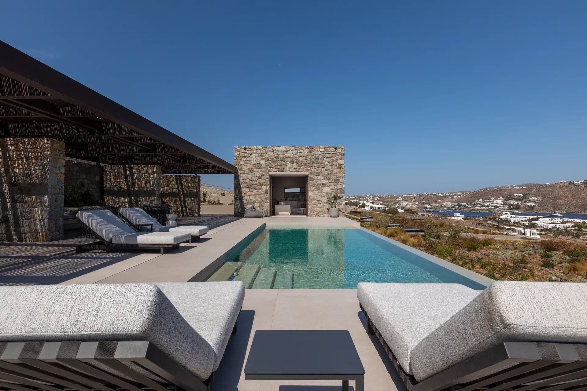 Infinity pool with sun loungers beneath a reed pergola overlooking the Aegean Sea