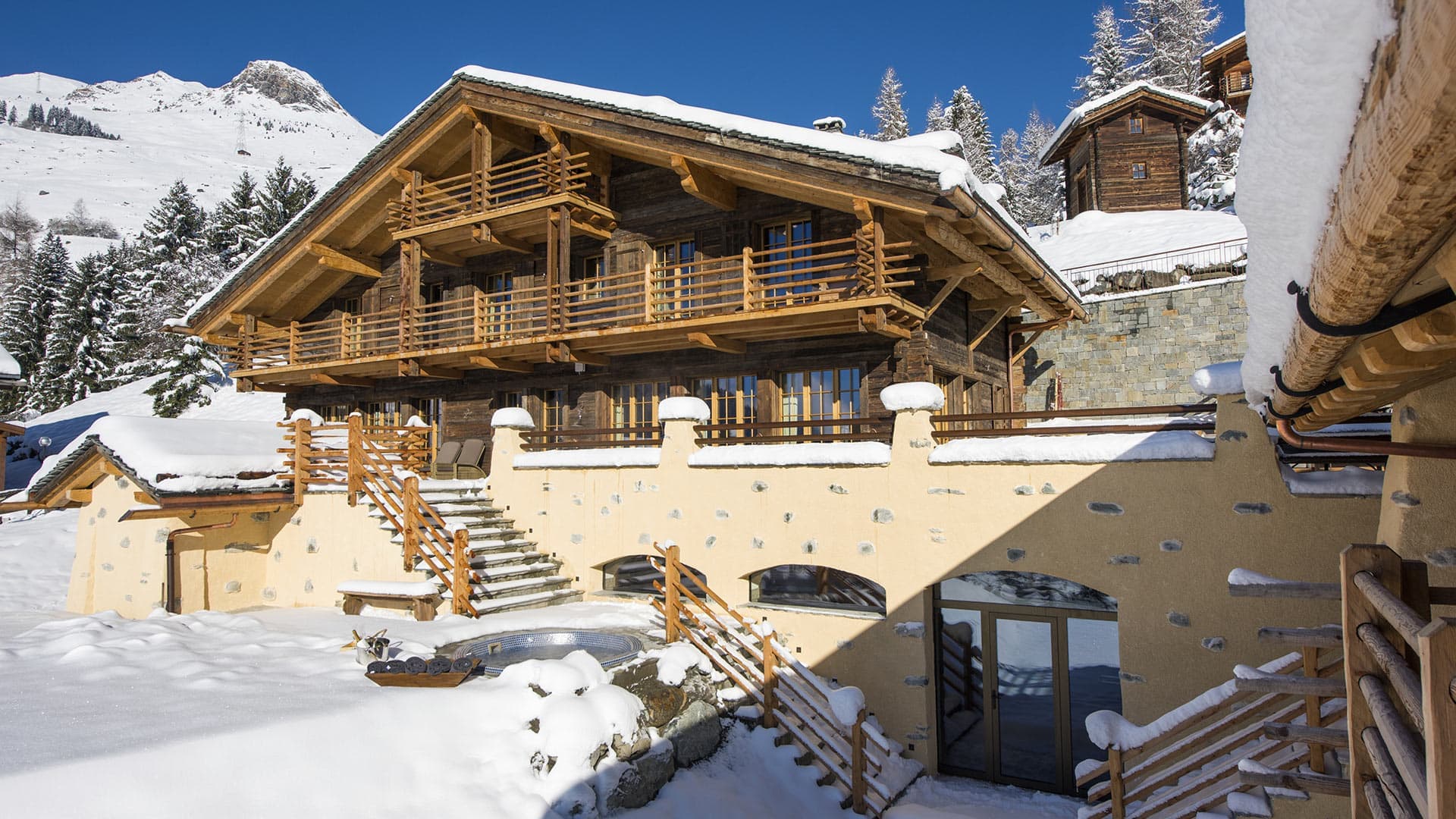 Snow-covered log chalet with stone base and balconies at Chalet On the Top, Verbier